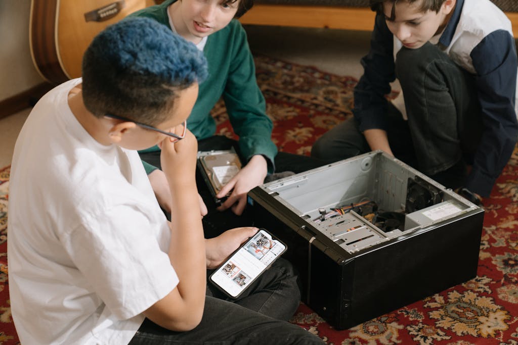 Three young boys repairing a computer indoors, focused and learning teamwork skills.